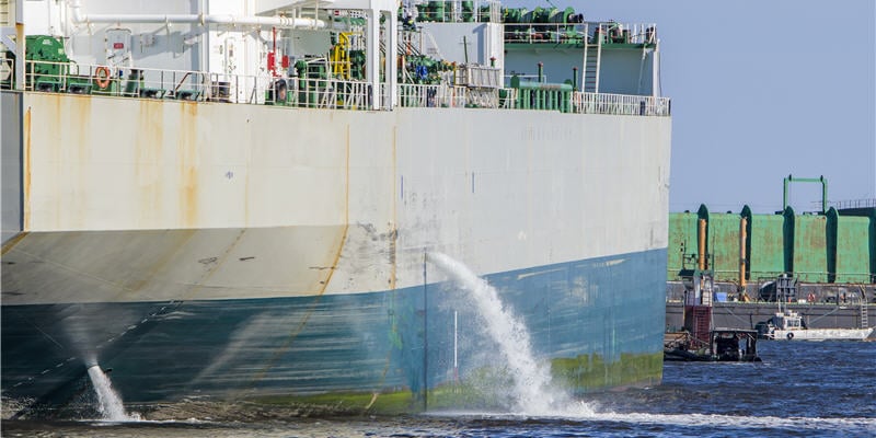 Tanker discharging ballast into the harbor. Water flows from the side. Ship not identifiable. Only part of ship visible (photo)