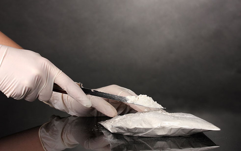 Packets of cocaine opening with a knife on grey background